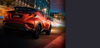TOYOTA C-HR Schrägansicht auf die Rückseite eines TOYOTA C-HR mit orange-rotem Lack. Der Neuwagen fährt nachts durch eine bunt beleuchtete Stadt. Ein drittel des Bildes wird mit einem grauen Balken überdeckt.