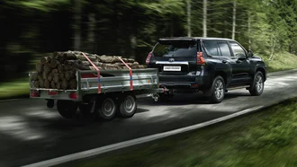 Toyota Land Cruiser mit einem mit Holz beladenen Anhänger auf einer Straße durch ein Waldstück