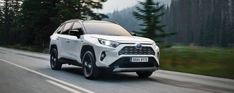 Weißer Toyota bei schönem Wetter auf einer Landstraße. Im Hintergrund sind Berge und Bäume zu sehen.