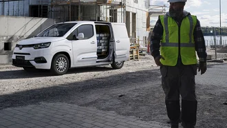 Weißer Toyota Proace City im Profil auf einer Baustelle, im Vordergrund läuft ein Bauarbeiter